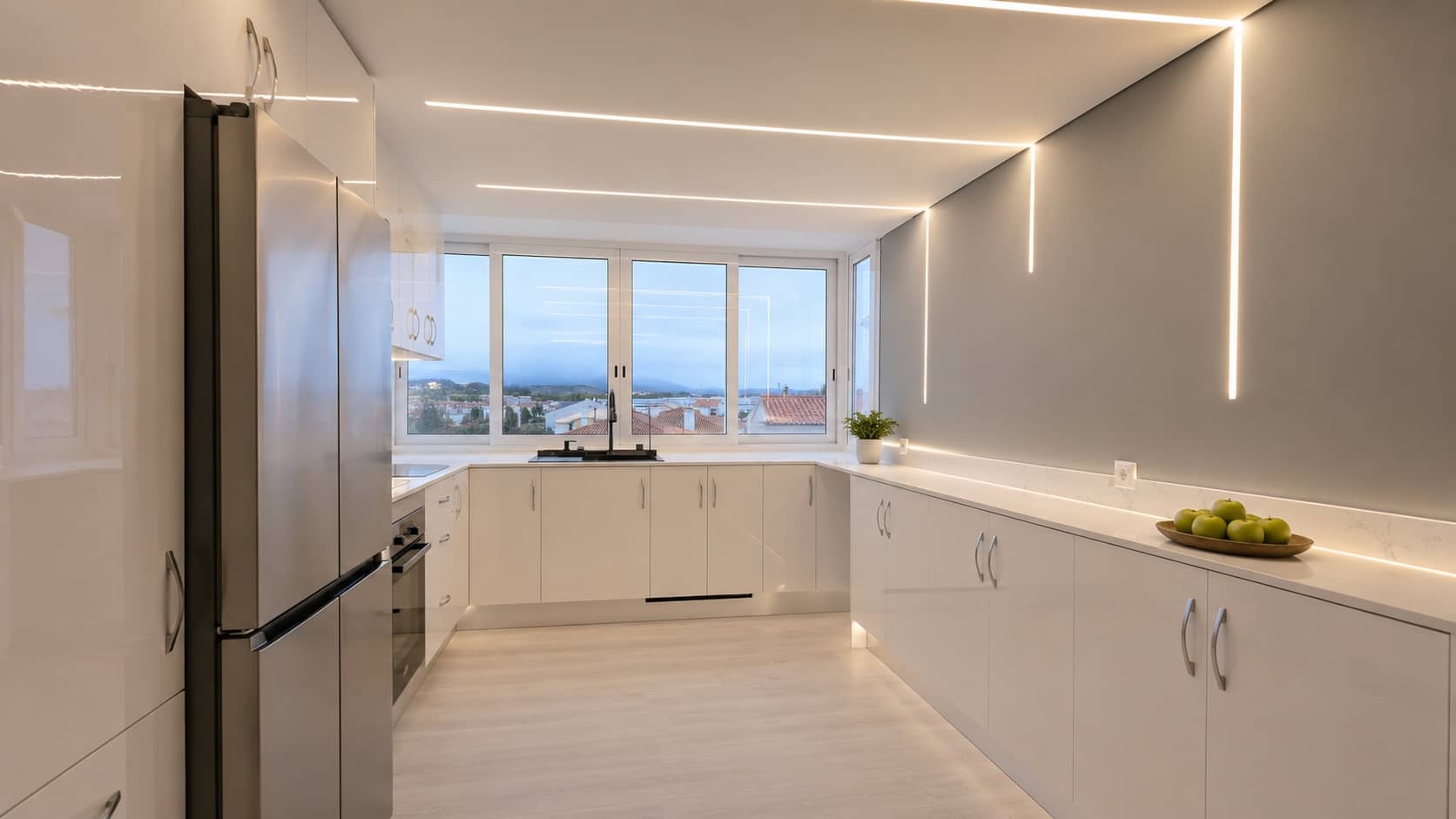 Cozinha branca minimalista com iluminação LED linear, frigorífico inox e vista panorâmica, obra da Alcance Flexível LDA